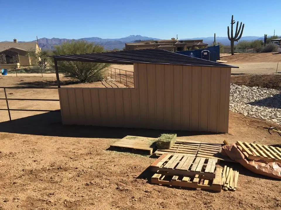 A tan Corral Kraft shed row on desert ground with mountains behind it and hay stacked on pallets alongside