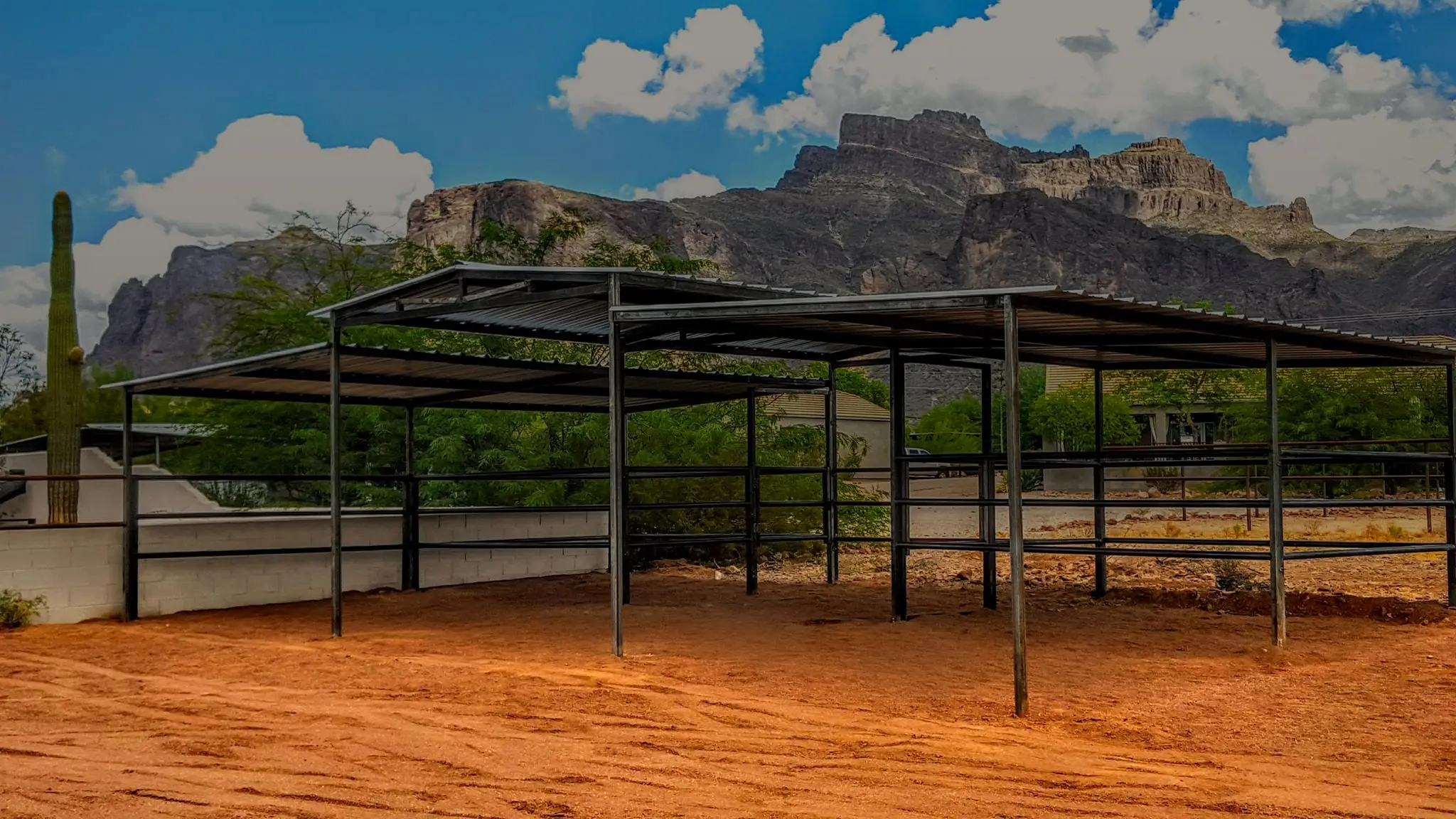 A steel shade and stall run built by Corral Kraft on red desert ground, with the Superstition Mountains behind it